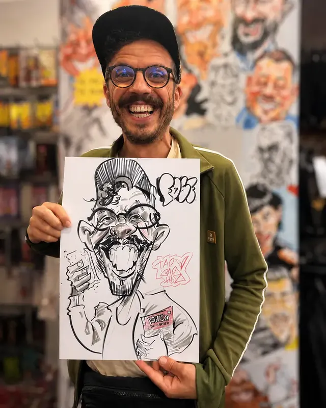 Un bărbat cu șapcă și ochelari, lângă caricatura lui